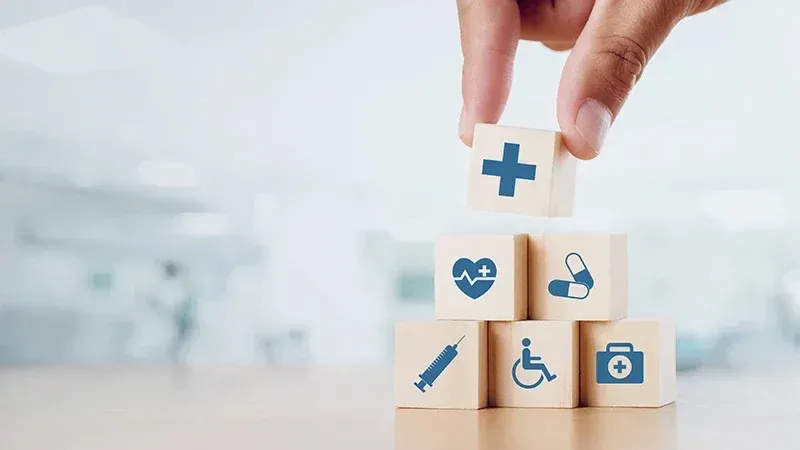 image of a hand stacking blocks that look like health care symbols